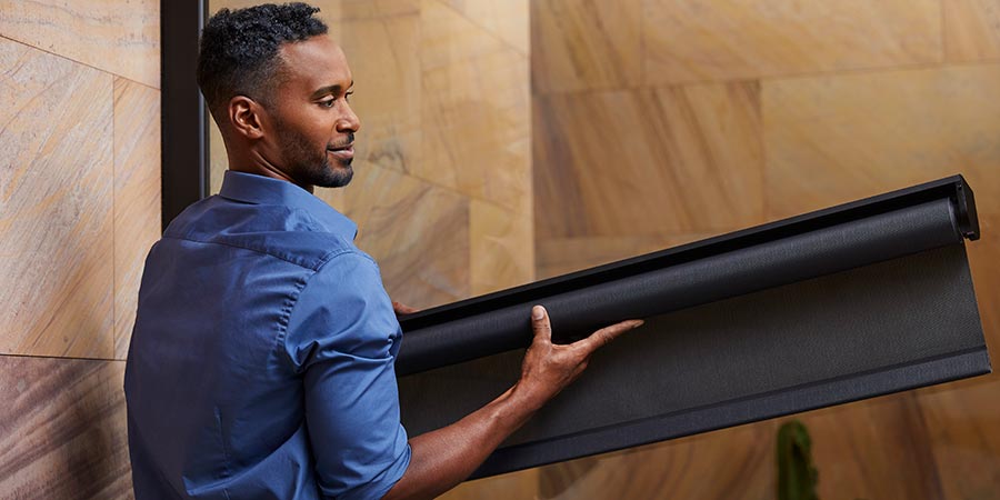 Man holding and installing a black motorized window shade