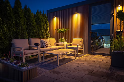 Outdoor patio at night with lounge furniture lit by warm wall lights