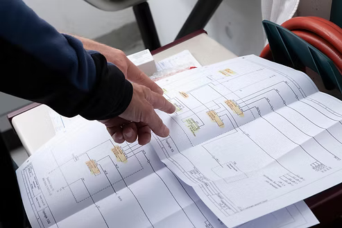 Hands pointing at printed system wiring plans spread on a table