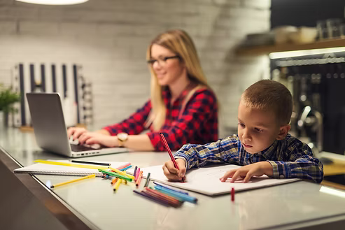 Woman working on a laptop while a child draws at a modern kitchen island