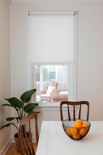 Dining area with white roller shade covering a window and a bowl of oranges on the table