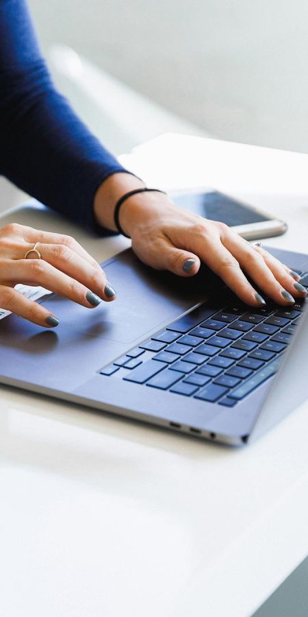 Person typing on a laptop keyboard resting on a white desk
