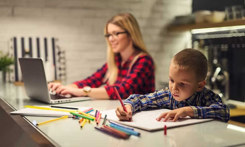 <span class="uk-h4">Woman working on a laptop while a child draws at a modern kitchen island</span>