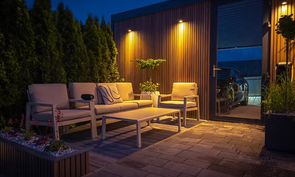 <span class="uk-h4">Outdoor patio at night with lounge furniture lit by warm wall lights</span>