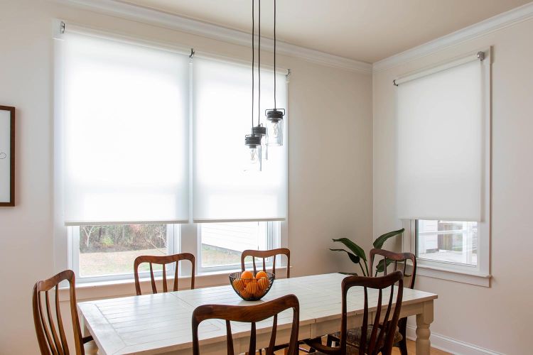 Bright dining room with white roller shades on multiple windows and pendant lights above the table