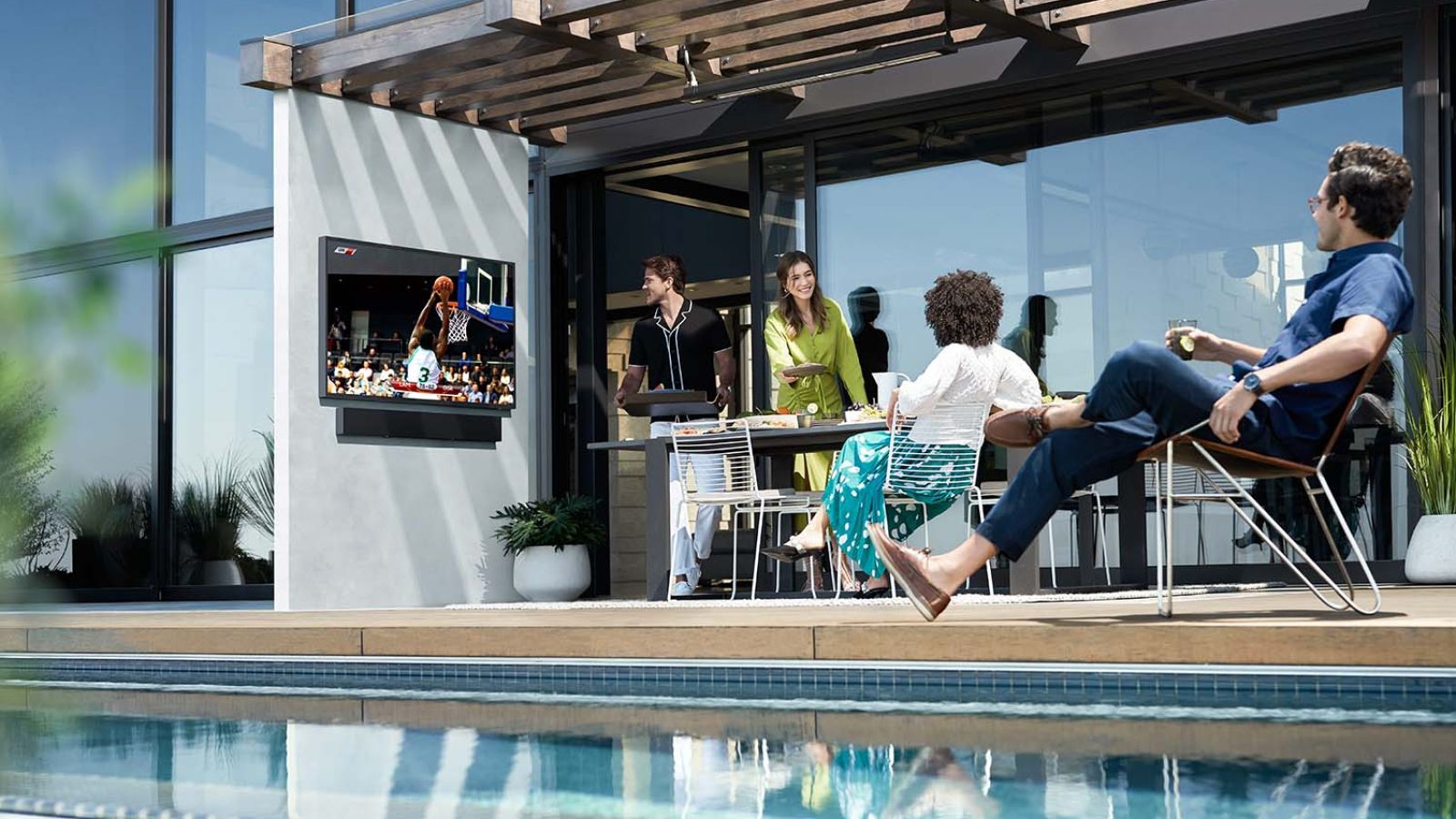 A group of people gathered enjoying a social gathering with outdoor seating, a fireplace, and a TV displaying a football game.