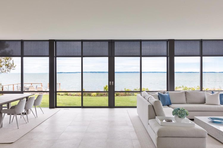 Modern living room with large windows and dark motorized shades overlooking the ocean